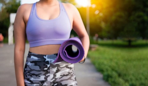 Unrecognizable woman holding a mat in the park. Athlete woman's hands carrying the mat after