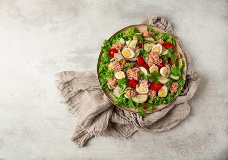 Tuna salad, vegetable salad with quail eggs, lettuce, red onion and cucumbers, on a light gray