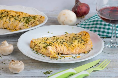 Savoury strudel with cheese and ham on a plate, alongside cutlery and a glass of red wine