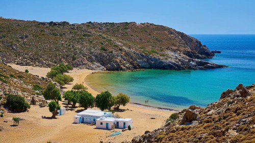 Secluded bay with clear water and golden sand, houses and trees, embedded in a rocky landscape