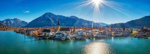 Panoramic shot of a village on the lake with mountains in the background, the sun shines on a clear