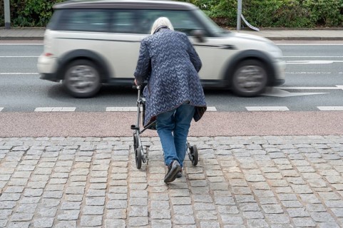 Elderly woman with rollator wants to cross the road, in front of her a passing car, Erlangen,