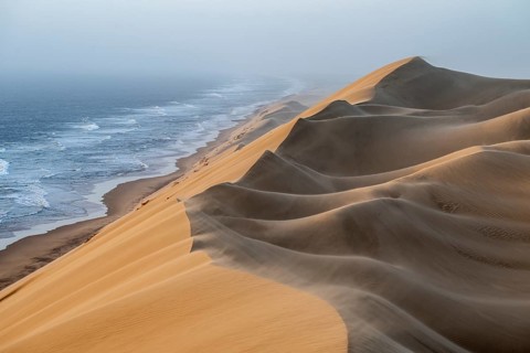 Sand dunes and sea in the evening light, wind blows sand over the dunes, view of the Atlantic coast