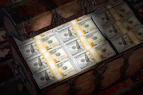 Flashlight shining on a treasure chest filled with millions of dollars in cash in a dark room