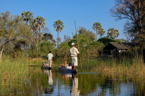 Tourists in a mokoro or dugout boat on safari in swamp area, Gomoti Plains Camp, Gomoti Concession