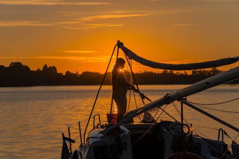 Silhouette of a woman on a sailing boat at sunset with orange sky, Lake Ilinsk, Jelonek, Milomlyn,
