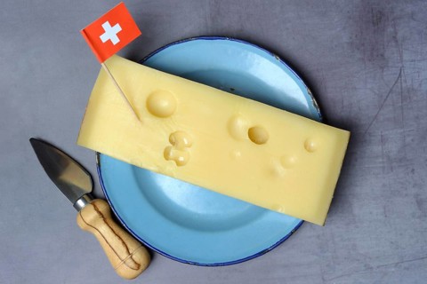 A piece of Swiss Emmental cheese on a plate and the Swiss flag