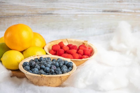 Blueberries, raspberries, oranges and lemons in wooden bowls, vitamin C, white background