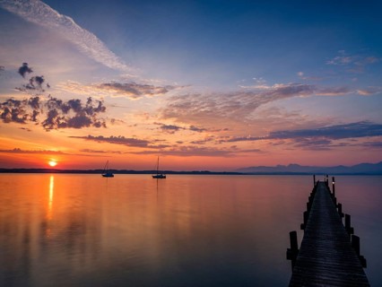 Sailing boats and jetty on Lake Chiemsee at sunrise, with the Chiemgau Alps in the background,