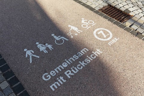 Mobility strip for walking speed in the pedestrian zone, marked with pictograms for pedestrians,