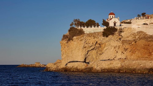 A small church on a rock above the sea in warm sunset light, Agios Nikolaos church, cemetery,