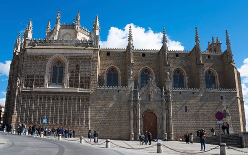 Large Gothic church with stone walls and towers under a blue sky, people standing in front of it,