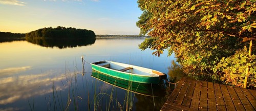 Quiet lake with jetty and rowing boat in the evening in autumn, horse chestnut with autumn leaves