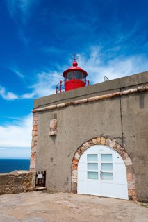 Round red lighthouse on a beige building with stone accents and blue sky in the background, Fort