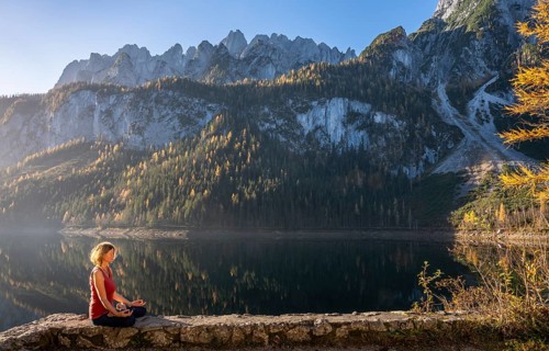A woman doing yoga by the lake. Lotus position (Padmasana) . Vorderer Gosausee in autumn with a