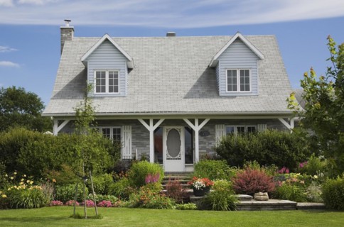 Facade of old grey nuanced brick with white trim cottage style Canadiana home with dormer windows