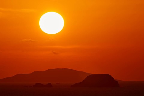 Intense sunset with a large, orange glowing sun over the ocean and islands, sunset, Kassos,