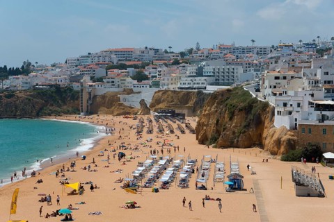 Lively sandy beach with lots of people and sun loungers in front of picturesque cliffs and a