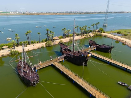 Wooden docks with replica medieval ships on the shore of a calm lake with palm trees in the