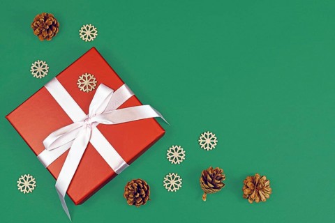Red Christmas gift box with ribbon surrounded by seasonal pine cones and wooden snowflake ornaments