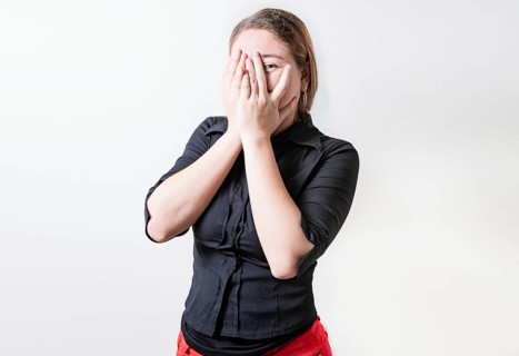 Embarrassed girl covering her face and looking at the camera. Shy girl covering her face and