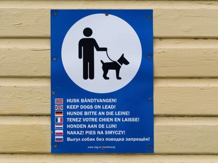 A multilingual sign instructing to keep dogs on a leash displayed on a wooden wall, Entrance to a