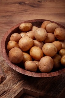 Small, unpeeled potatoes gathered together in a rustic wooden bowl, highlighting their earthy