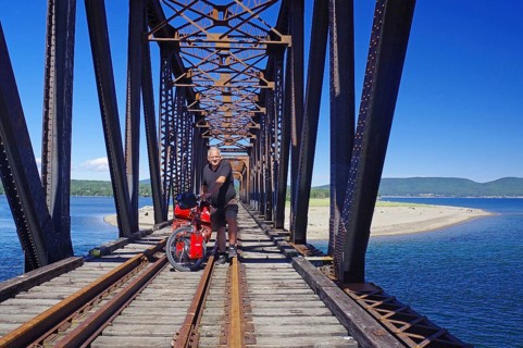 A railway bridge crossed by a person on a bicycle over the sea, surrounded by nature and blue
