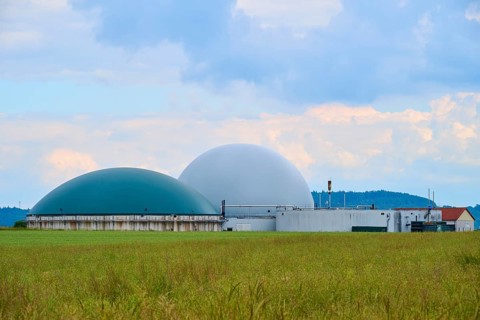 Modern biogas plant in the middle of green fields under a cloudy blue sky, summer, Middle