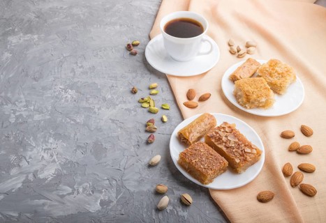 Traditional arabic sweets (basbus, kunafa, baklava) and a cup of coffee on a gray concrete
