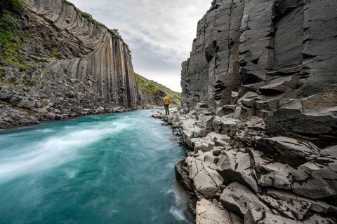 Tourist standing by the river in Stuðlagil Canyon, turquoise blue river between basalt columns,