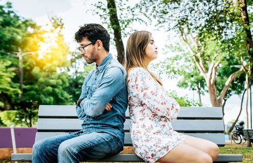 Upset young couple sitting back to back in a park, unhappy couple sitting back to back on bench.