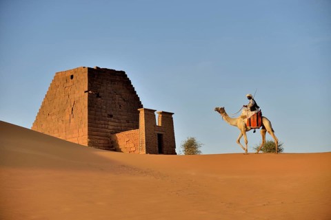 Man riding a dromedar in front of a pyramid of the northern cemetery of Meroe, Nubia, Nahr an-Nil,