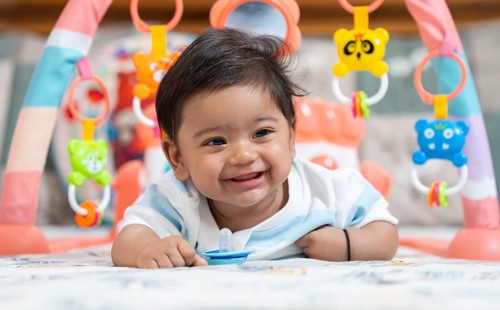 Baby boy playing and smiles lying on bed with pacifier on mouth