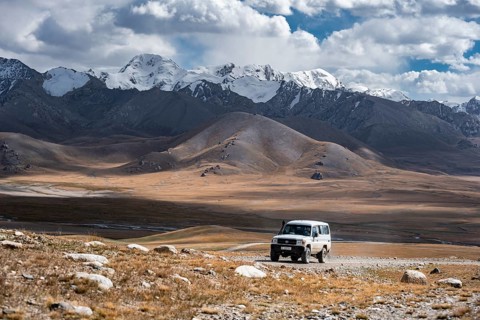 Off-road vehicle on a gravel track, glaciated and snow-covered peaks, Ak Shyrak Mountains, near