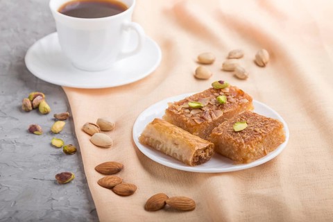 Traditional arabic sweets (basbus, kunafa, baklava) and a cup of coffee on a gray concrete
