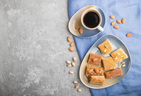 Traditional arabic sweets (basbus, kunafa, baklava) and a cup of coffee on a gray concrete