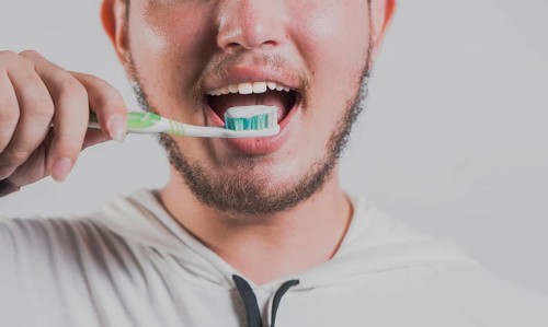 Health and tooth brushing concept. Smiling man brushing teeth isolated