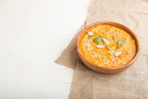 Sweet potato or batata cream soup with sesame seeds in a wooden bowl on a white wooden background