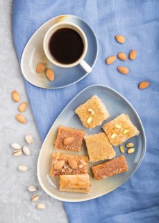 Traditional arabic sweets (basbus, kunafa, baklava) and a cup of coffee on a gray concrete