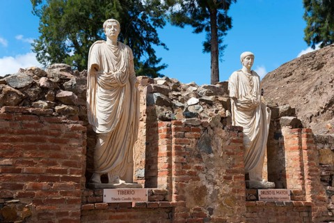 Two Roman statues made of stone, with name plaques, embedded in ancient brick structures and trees