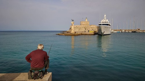 A man fishing on a shore with a view of an old fortress and a luxury yacht at sunset, Fort of Saint