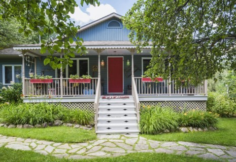 Blue and tan country cottage style residential home facade with veranda in summer, Quebec, Canada,