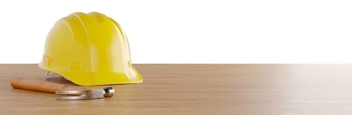 Yellow construction hard hat and hammer resting on wood surface banner isolated on a white