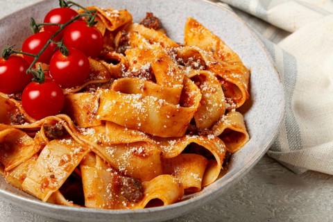 Pappardelle pasta with bolognese sauce, topped with parmesan cheese and cherry branch, homemade, no