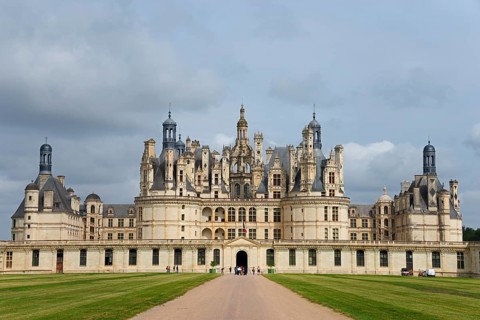 Historic castle with imposing architecture and elaborate towers under a cloudy sky, surrounded by a