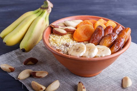 A plate with muesli, banana, dried apricots, dates, Brazil nuts on a black wooden background. close