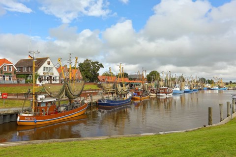 View of historic houses with colourful facades at the old harbour of Greetsiel, with fishing boat,
