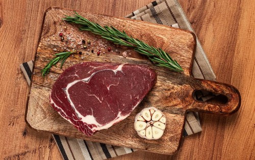 Raw steak, beef steak, rib eye steak, on a cutting board, freshly frozen, with spices and herbs, on