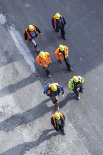 Several construction workers wearing hard hats walk over tarmac. They cast long shadows. Stuttgart,